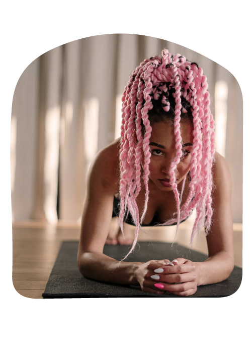 woman with vibrant, pink hair in a plank position on a yoga mat, her hands folded as she practices for her yoga teacher certification in san francisco